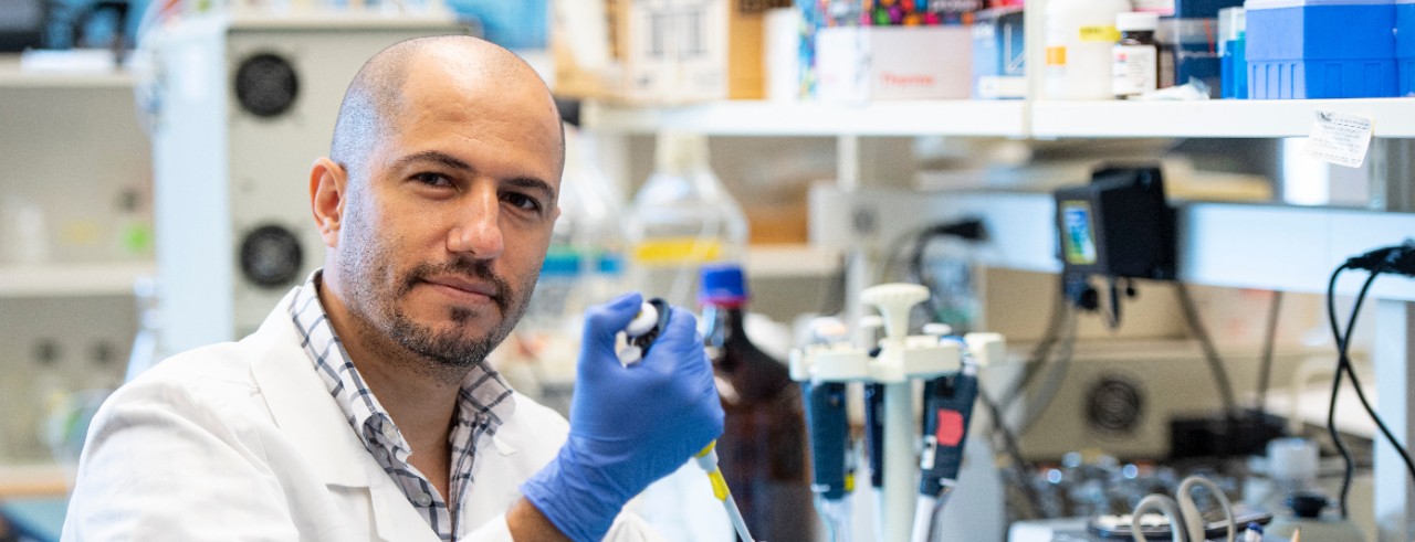 Ahmet Kaynak in a white lab coat holding a test tube in a lab