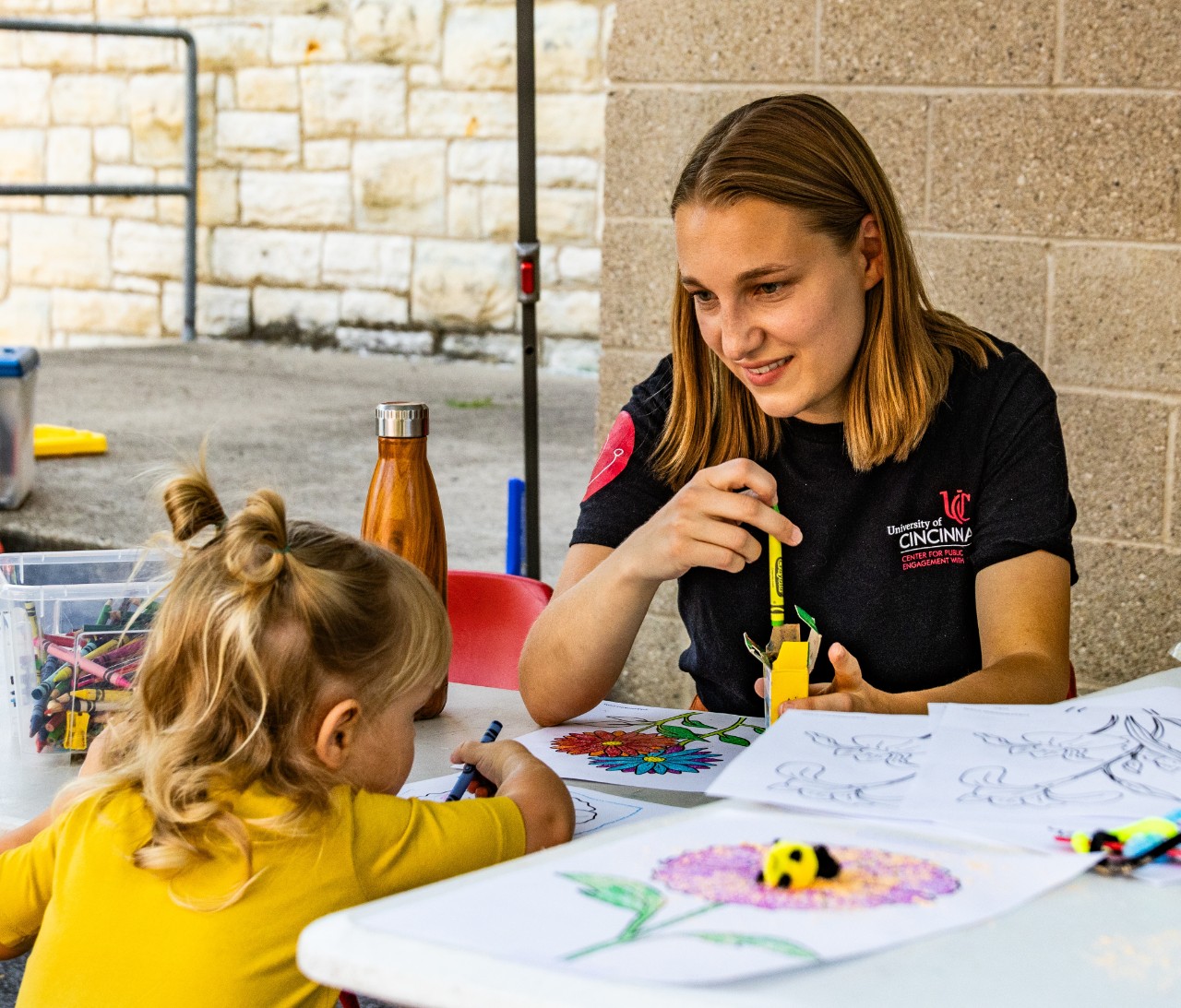 UC student researcher helps little learner understand pollination at Northside Farmers Market. 