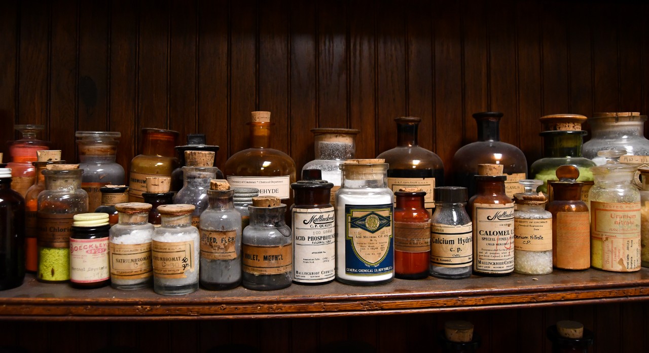 A row of chemical bottles on a wooden shelf.
