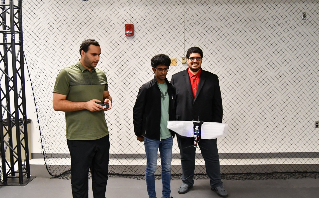 Three people watch a flapper drone fly in a flight cage.