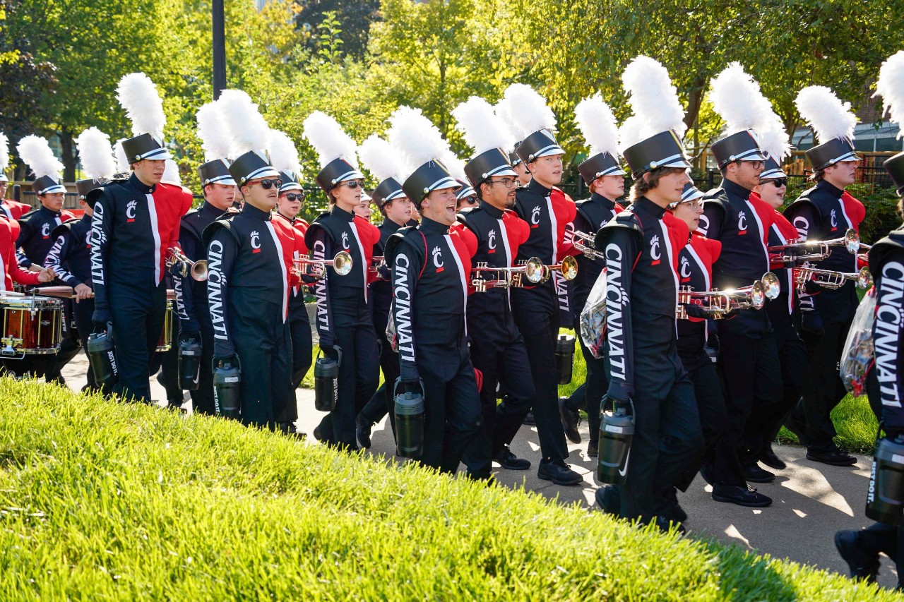 Several members of the marching bandwalk with trumpets and all dressed in UC attire