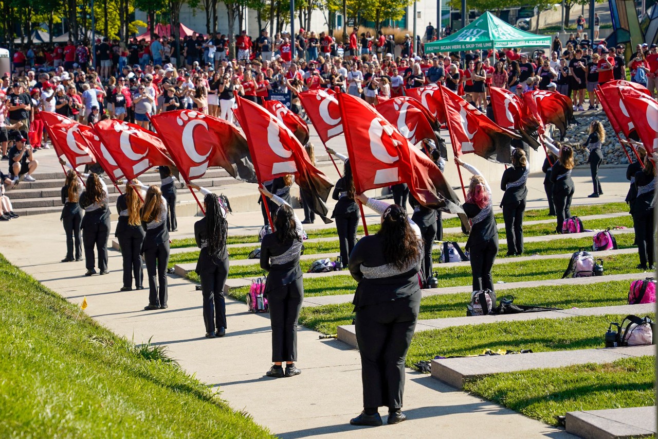 More than a dozen young women hold UC flag and perform before a crowd of hundreds