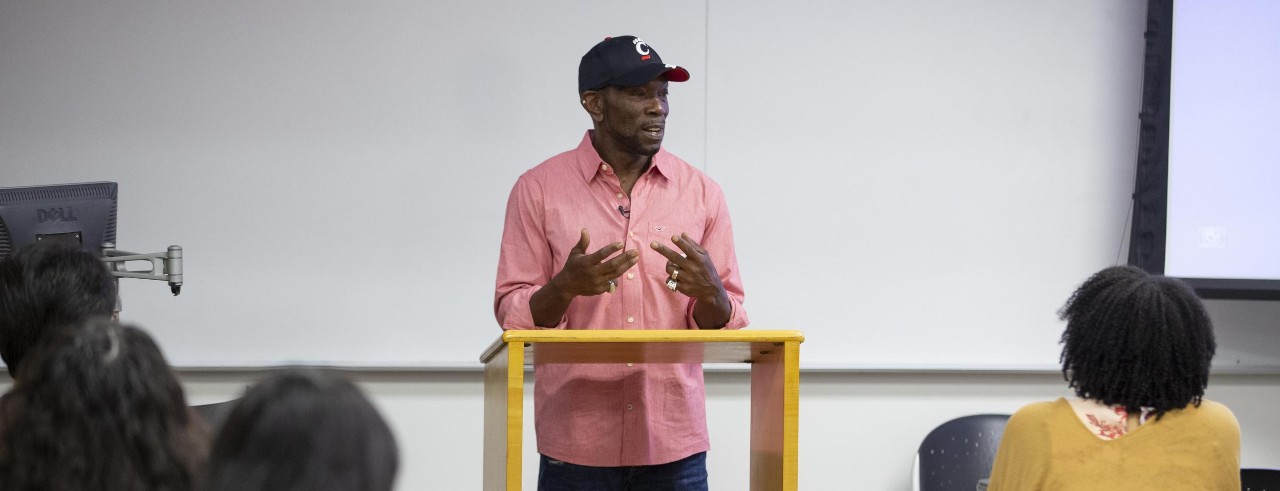 Rickey Jackson stands at podium wearing a Bearcats hat and speaks to UC Law students