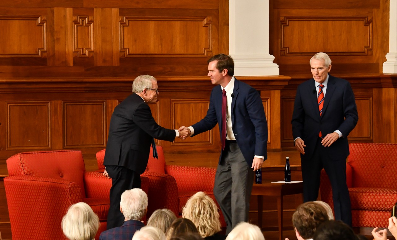 Mike DeWine and Andy Beshear shake hands on stage at UC's Probasco Auditorium.