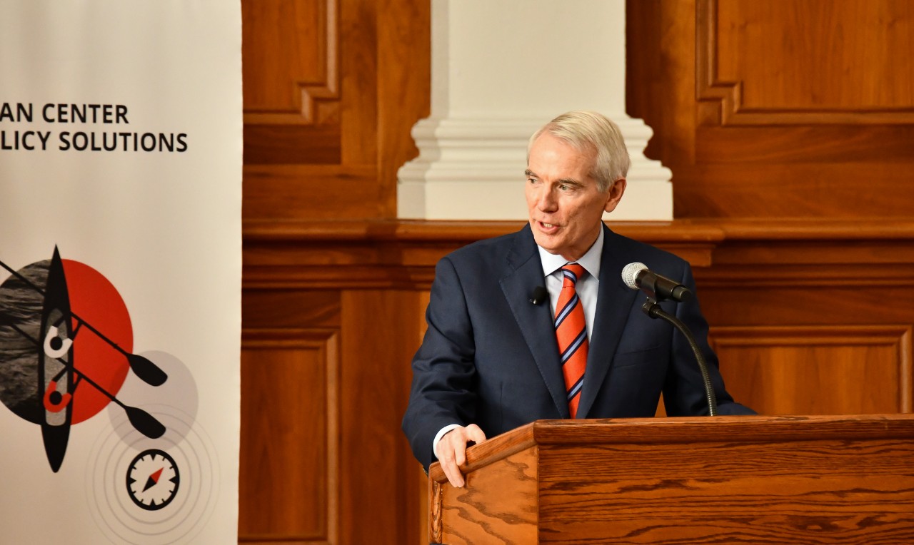 Rob Portman talks at a dais in front of a banner for the Portman Center for Policy Solutions.