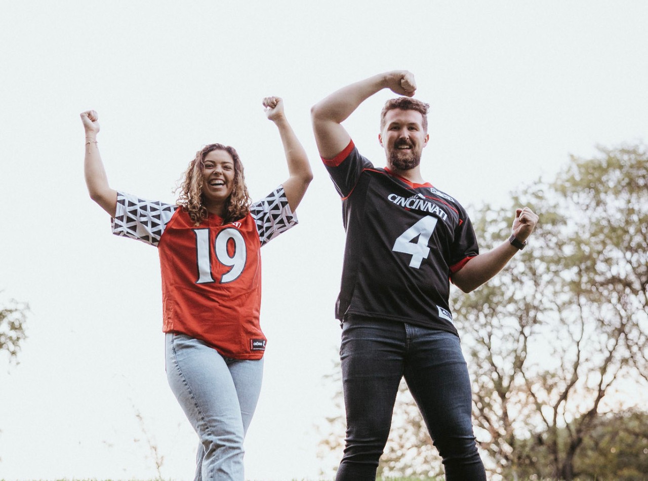 Annelise Atkinson and partner form "U" and "C" with arms while sporting Cincinnati Bearcats football jerseys