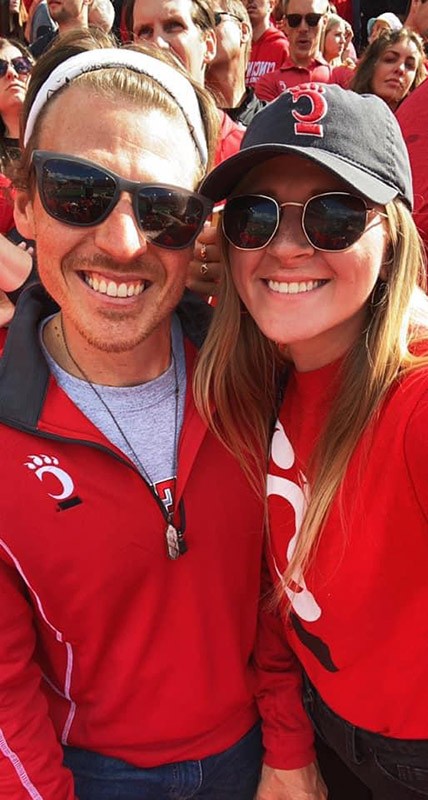 Abby Revetta and partner pose in UC gear at a Cincinnati Bearcats football game
