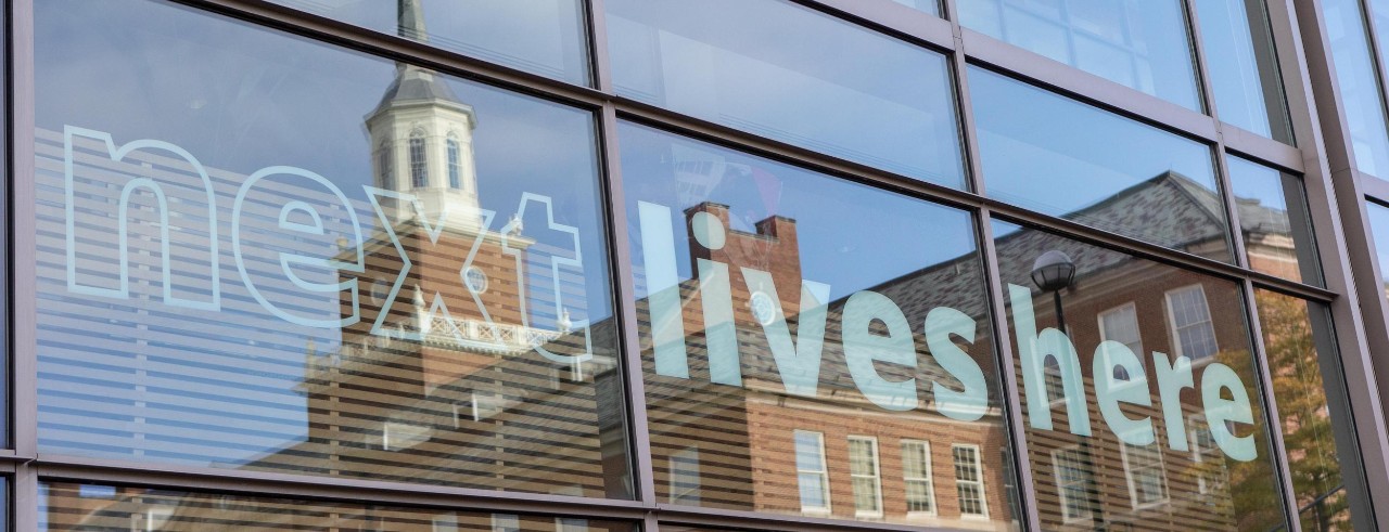 Next Lives Here reflected on a window on UC's campus