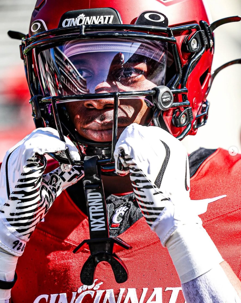 A football player grabs his facemask while staring intently at the field.